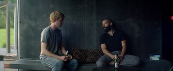 Movie still from “Ex Machina” (2014), directed by Alex Garland – Two men are sitting on a couch and one of them has a beer in his hand; Medium shot, Over the shoulder angle