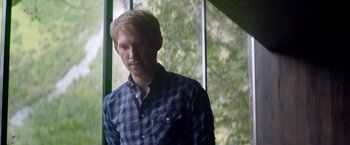 Movie still from “Ex Machina” (2014), directed by Alex Garland – A man standing in front of a window with trees in the background; Medium shot, Over the shoulder angle