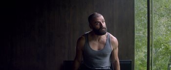 Movie still from “Ex Machina” (2014), directed by Alex Garland – A man with a goatee and a beard is sitting in front of a wooden wall; Medium shot, Over the shoulder angle