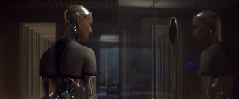 Movie still from “Ex Machina” (2014), directed by Alex Garland – A woman is standing in front of a glass window; Close Up shot, Over the shoulder angle