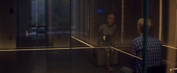 Movie still from “Ex Machina” (2014), directed by Alex Garland – A robot sitting in a glass case in a dark room; Wide shot, High angle