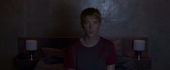 Movie still from “Ex Machina” (2014), directed by Alex Garland – A young man is sitting in a dark room; Medium shot, Over the shoulder angle