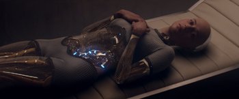 Movie still from “Ex Machina” (2014), directed by Alex Garland – A woman in a body suit is laying on the ground; Medium shot, High angle