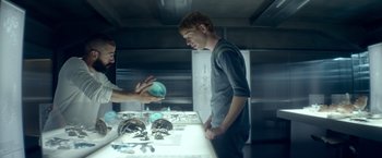Movie still from “Ex Machina” (2014), directed by Alex Garland – Two people are looking at some items on a table; Medium shot, Over the shoulder angle