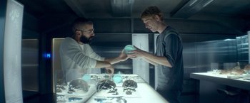 Movie still from “Ex Machina” (2014), directed by Alex Garland – Two men in a room with a table and a refrigerator; Medium shot, Over the shoulder angle