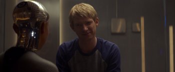 Movie still from “Ex Machina” (2014), directed by Alex Garland – A man with blonde hair wearing a blue and white raglan t - shirt; Close Up shot, Over the shoulder angle