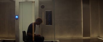 Movie still from “Ex Machina” (2014), directed by Alex Garland – A man sitting on the ground in front of a glass wall; Wide shot, High angle