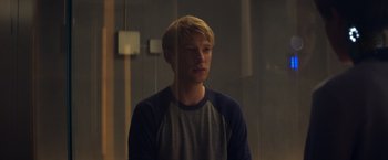 Movie still from “Ex Machina” (2014), directed by Alex Garland – A young man standing in front of a glass wall; Medium shot, Over the shoulder angle