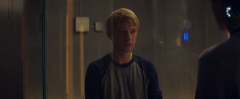 Movie still from “Ex Machina” (2014), directed by Alex Garland – A young blond haired man wearing a blue and white shirt; Medium shot, Over the shoulder angle