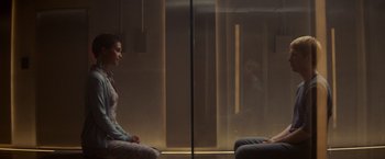 Movie still from “Ex Machina” (2014), directed by Alex Garland – A woman sitting in front of a glass window; Wide shot, Over the shoulder angle
