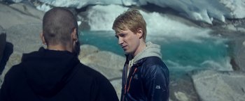 Movie still from “Ex Machina” (2014), directed by Alex Garland – A man standing next to another man near a body of water; Close Up shot, Over the shoulder angle