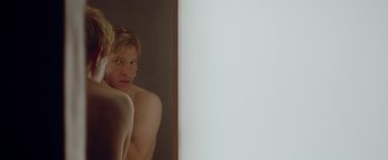 Movie still from “Ex Machina” (2014), directed by Alex Garland – A shirtless man looking into a bathroom mirror; Medium shot, Over the shoulder angle