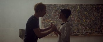 Movie still from “Ex Machina” (2014), directed by Alex Garland – A man and a woman holding hands in front of a painting; Medium shot, High angle