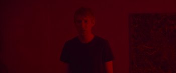 Movie still from “Ex Machina” (2014), directed by Alex Garland – A man in a black shirt is standing in a red room; Close Up shot, Low angle