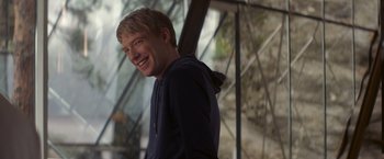 Movie still from “Ex Machina” (2014), directed by Alex Garland – A young man smiling while standing in front of a window; Medium shot, Over the shoulder angle