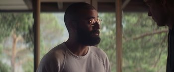 Movie still from “Ex Machina” (2014), directed by Alex Garland – A man with a goatee wearing glasses and a white t - shirt; Close Up shot, Over the shoulder angle