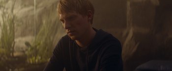 Movie still from “Ex Machina” (2014), directed by Alex Garland – A man with blonde hair sitting in a dark room; Close Up shot, Over the shoulder angle