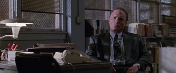 Movie still from “Glengarry Glen Ross” (1992), directed by James Foley – A man sitting at a desk in a suit and tie; Medium shot, Low angle