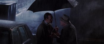 Movie still from “Glengarry Glen Ross” (1992), directed by James Foley – Two men standing under an umbrella in the rain; Medium shot, Over the shoulder angle