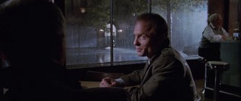 Movie still from “Glengarry Glen Ross” (1992), directed by James Foley – A man sitting at a table in front of a window; Medium shot, Over the shoulder angle