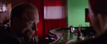 Movie still from “Glengarry Glen Ross” (1992), directed by James Foley – A man sitting at a table in front of a red curtain; Medium shot, Over the shoulder angle