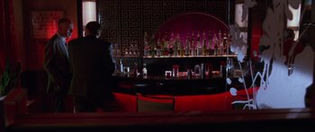 Movie still from “Glengarry Glen Ross” (1992), directed by James Foley – A man walking in front of a bar filled with bottles; Wide shot, High angle