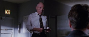 Movie still from “Glengarry Glen Ross” (1992), directed by James Foley – An older man holding a cell phone while standing in a dark room; Medium shot, Low angle