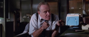 Movie still from “Glengarry Glen Ross” (1992), directed by James Foley – An older man sitting in a chair wearing a tie; Close Up shot, Low angle