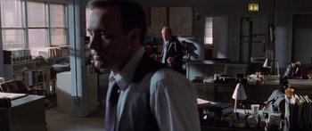 Movie still from “Glengarry Glen Ross” (1992), directed by James Foley – A man in a suit and tie standing in front of another man in a suit and tie; Medium shot, Over the shoulder angle
