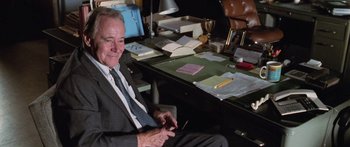 Movie still from “Glengarry Glen Ross” (1992), directed by James Foley – An older man sitting at a desk looking at a phone; Medium shot, High angle