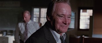 Movie still from “Glengarry Glen Ross” (1992), directed by James Foley – An older man wearing a suit and tie in a room; Close Up shot, Over the shoulder angle