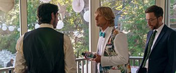 Movie still from “Father Figures” (2017), directed by Lawrence Sher – A man in a suit and tie holding a bottle of wine; Medium shot, Over the shoulder angle