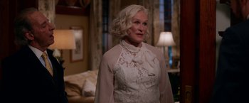 Movie still from “Father Figures” (2017), directed by Lawrence Sher – An older woman wearing a white dress in a living room; Medium shot, Over the shoulder angle