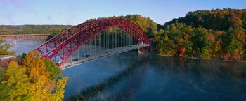 Movie still from “Father Figures” (2017), directed by Lawrence Sher – A red and white bridge over a body of water near a forest; Extreme Wide shot, High angle