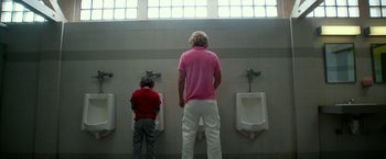 Movie still from “Father Figures” (2017), directed by Lawrence Sher – Two people standing in front of urinals in a bathroom; Wide shot, Low angle
