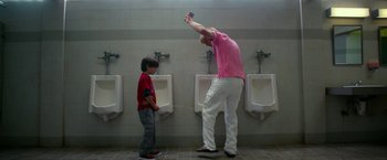 Movie still from “Father Figures” (2017), directed by Lawrence Sher – A man and a boy are standing in front of urinals in a bathroom; Wide shot, Low angle