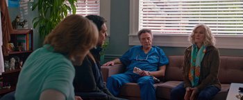 Movie still from “Father Figures” (2017), directed by Lawrence Sher – A man sitting on top of a brown couch next to two other people; Medium shot, Over the shoulder angle