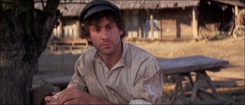 Movie still from “Fiddler on the Roof” (1971), directed by Norman Jewison – A man wearing a hat sitting in front of a building; Close Up shot, Low angle