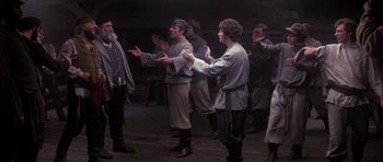 Movie still from “Fiddler on the Roof” (1971), directed by Norman Jewison – A group of men standing around each other in a room; Wide shot, Low angle
