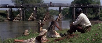 Movie still from “Fiddler on the Roof” (1971), directed by Norman Jewison – A group of people sitting in the grass near a river; Wide shot, High angle