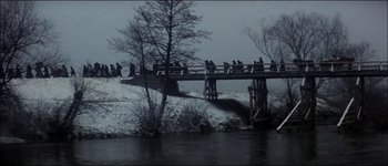 Movie still from “Fiddler on the Roof” (1971), directed by Norman Jewison – A group of people sitting on a bridge over a body of water; Extreme Wide shot, High angle