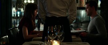 Movie still from “Fifty Shades Darker” (2017), directed by James Foley – A person standing at a table with a wine glass on it; Medium shot, Over the shoulder angle