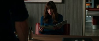 Movie still from “Fifty Shades Darker” (2017), directed by James Foley – A woman sitting at a table looking at a book; Medium shot, Over the shoulder angle