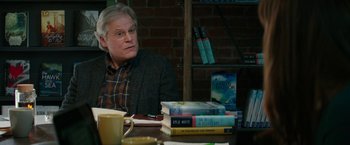 Movie still from “Fifty Shades Darker” (2017), directed by James Foley – A man sitting at a table with a stack of books; Medium shot, Over the shoulder angle