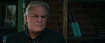 Movie still from “Fifty Shades Darker” (2017), directed by James Foley – An older man wearing glasses sitting in front of a brick wall; Close Up shot, Over the shoulder angle