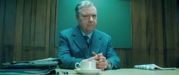 Movie still from “Filth” (2013), directed by Jon S. Baird – An older man sitting at a table in front of a coffee cup; Medium shot, Low angle