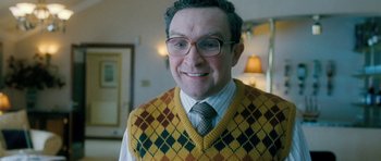Movie still from “Filth” (2013), directed by Jon S. Baird – A person wearing glasses and a sweater vest; Close Up shot, Low angle
