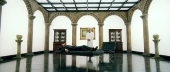 Movie still from “Filth” (2013), directed by Jon S. Baird – A man laying on a couch in a room with a man standing next to him; Wide shot, High angle