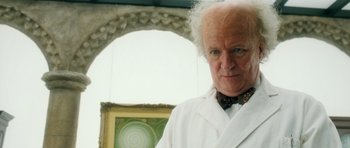 Movie still from “Filth” (2013), directed by Jon S. Baird – An older man in a white lab coat and bow tie; Close Up shot, Low angle