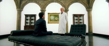 Movie still from “Filth” (2013), directed by Jon S. Baird – A man and a man in a lab coat talking to each other in a room; Wide shot, Over the shoulder angle
